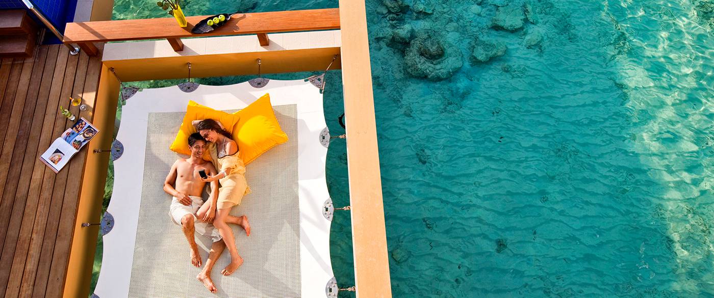 Couple enjoying their vacation on overwater hammock with Vacation Maldives
