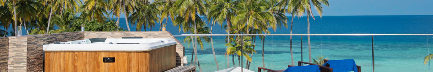 Views of a private Jacuzzi with sun beds overlooking shallow bluish sea in Maldives