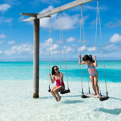 two guests enjoying an over water swing in Maldives shallow water