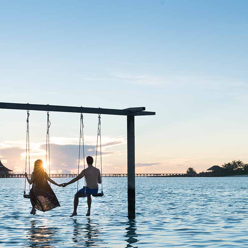 Couple enjoying vacation in overwater swing at Maldives